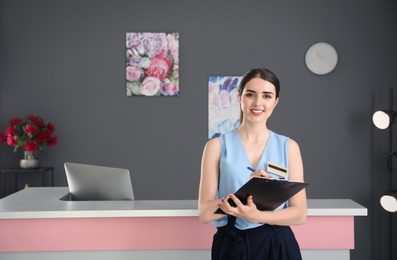 Young receptionist with clipboard at desk in beauty salon
