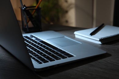 Silver laptop, notebook and pen on dark wooden table indoors, closeup