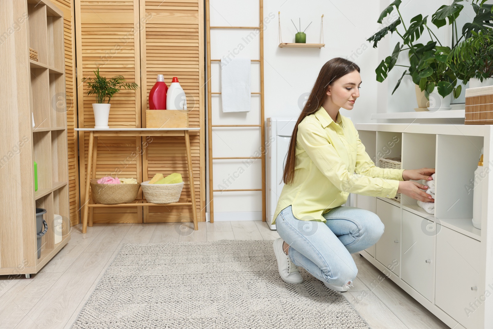 Photo of Beautiful young woman taking towels from drawer in laundry room