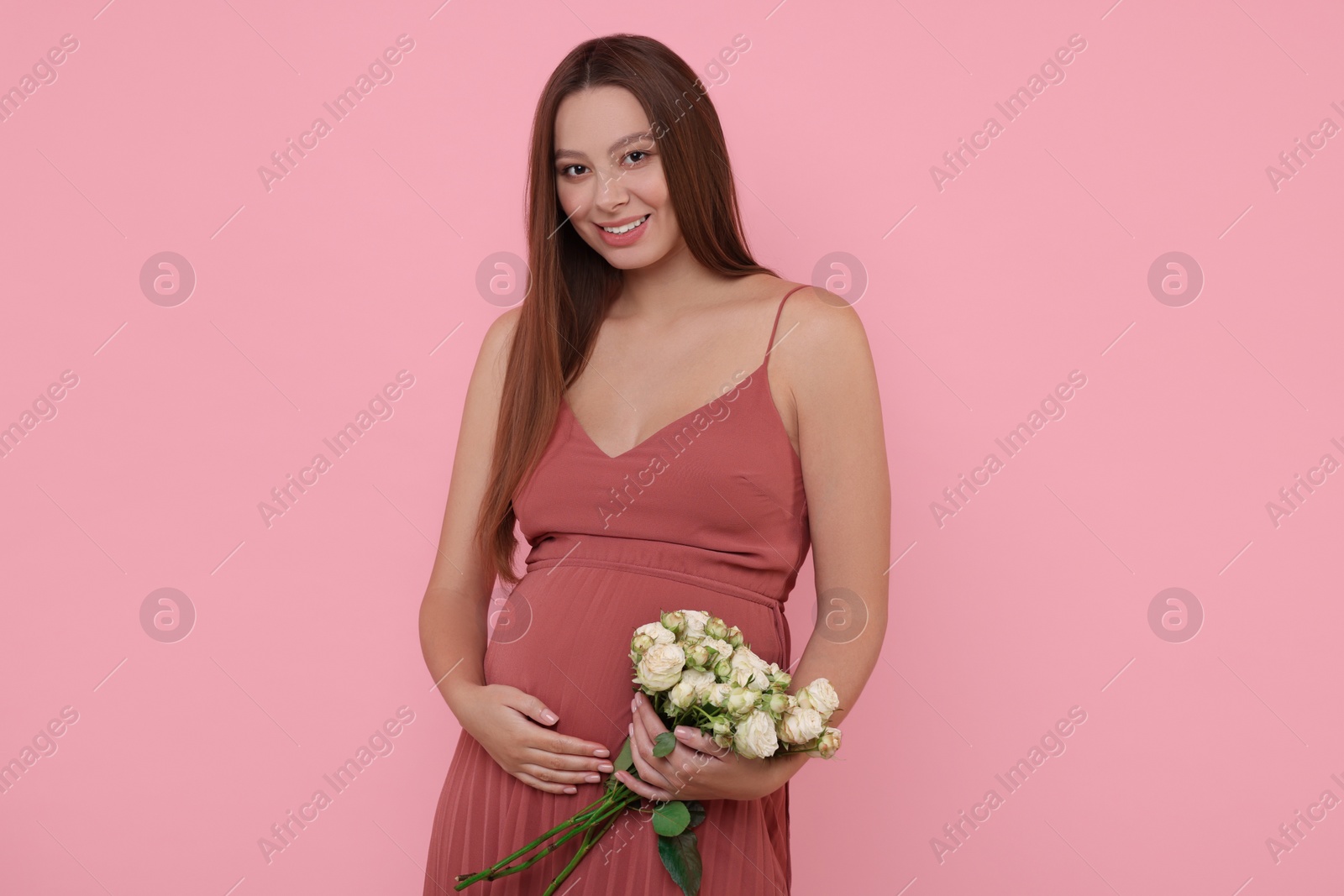 Photo of Beautiful pregnant woman in dress with bouquet of roses on pink background