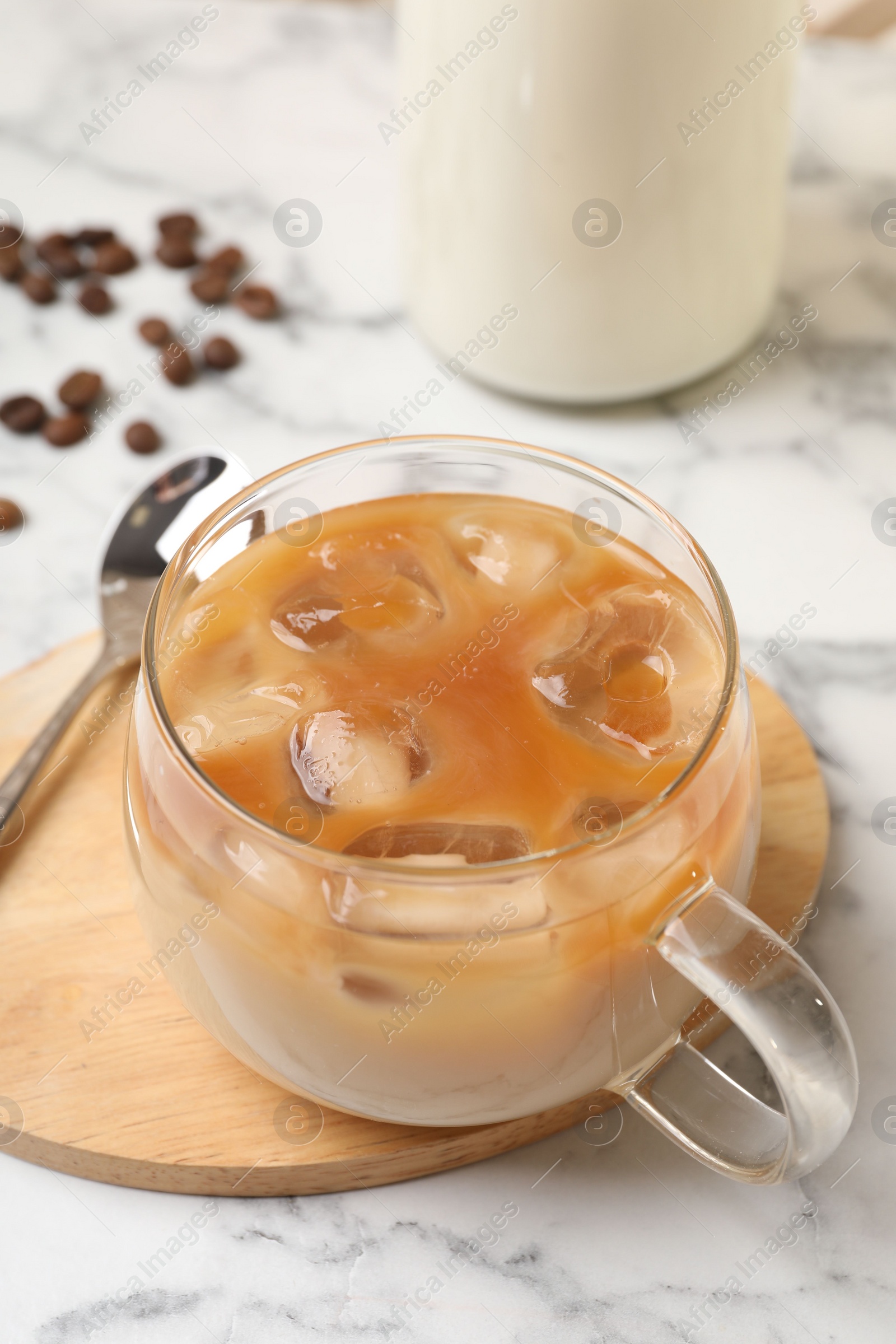 Photo of Refreshing iced coffee with milk in glass cup on white marble table, closeup