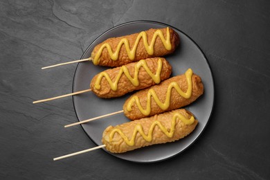Delicious deep fried corn dogs with mustard on black table, top view