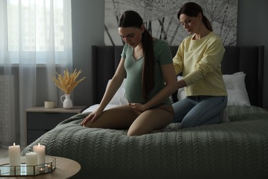 Doula massaging pregnant woman in bedroom. Preparation for child birth