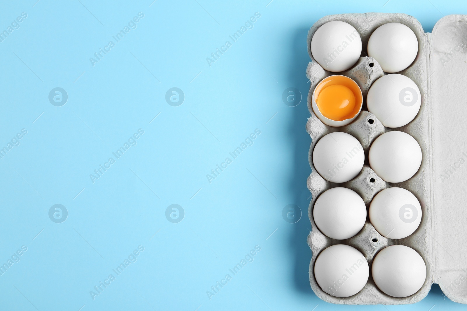 Photo of Fresh chicken eggs in box on light blue background, top view. Space for text