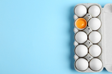 Photo of Fresh chicken eggs in box on light blue background, top view. Space for text