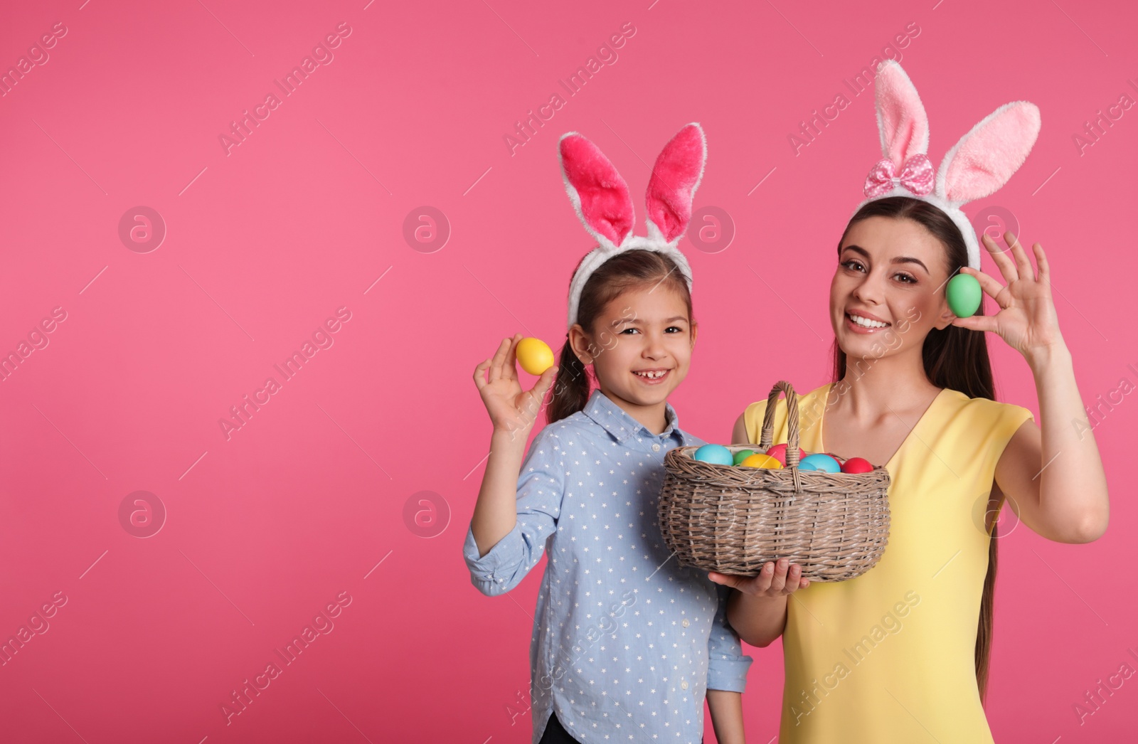 Photo of Mother and daughter in bunny ears headbands with Easter eggs on color background, space for text