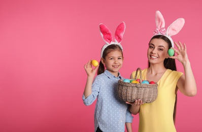 Photo of Mother and daughter in bunny ears headbands with Easter eggs on color background, space for text