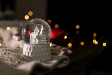 Photo of Christmas snow globe with knitting clothes on blurred background. Space for text