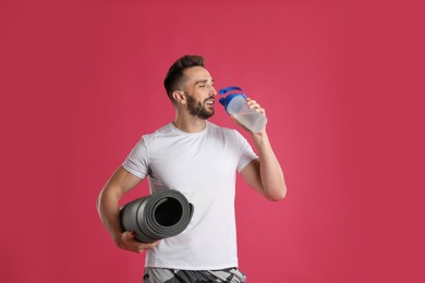 Photo of Handsome man with yoga mat drinking water on pink background