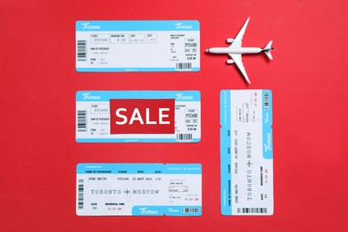 Photo of Flight tickets, plane model and SALE card on red background, flat lay