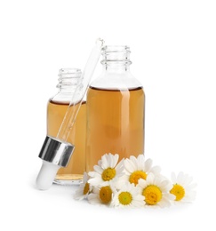 Photo of Chamomile flowers and cosmetic bottles of essential oil on white background