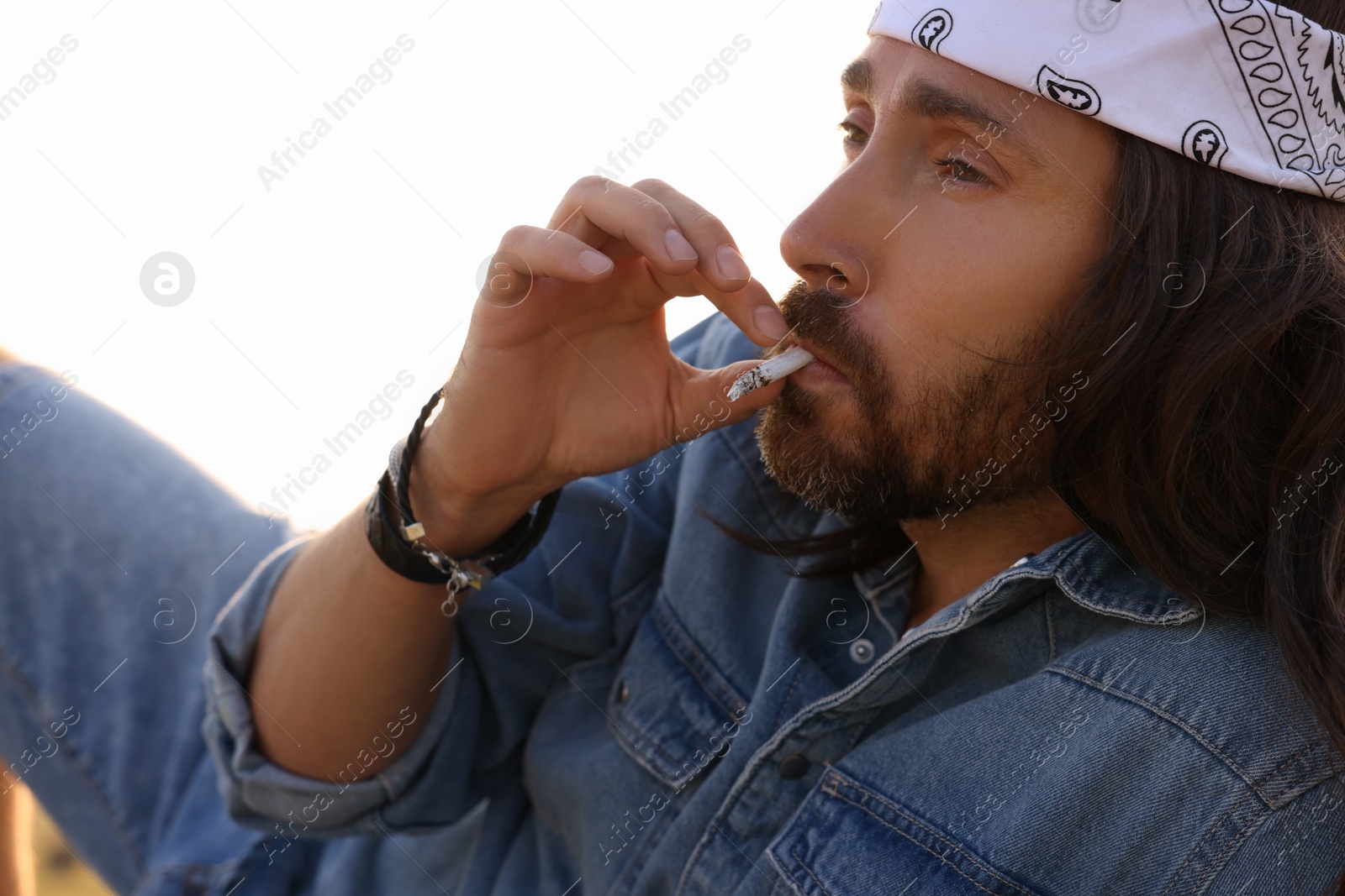 Photo of Hippie man in headband smoking joint outdoors