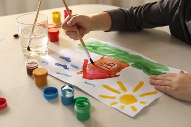 Little boy drawing picture with brush at wooden table indoors, closeup. Child`s art