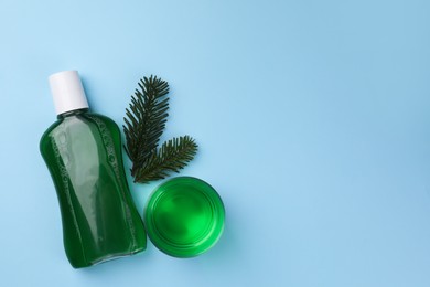 Fresh mouthwash in bottle, glass and fir branches on light blue background, flat lay. Space for text