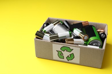 Image of Used batteries in cardboard box with recycling symbol on yellow background, space for text