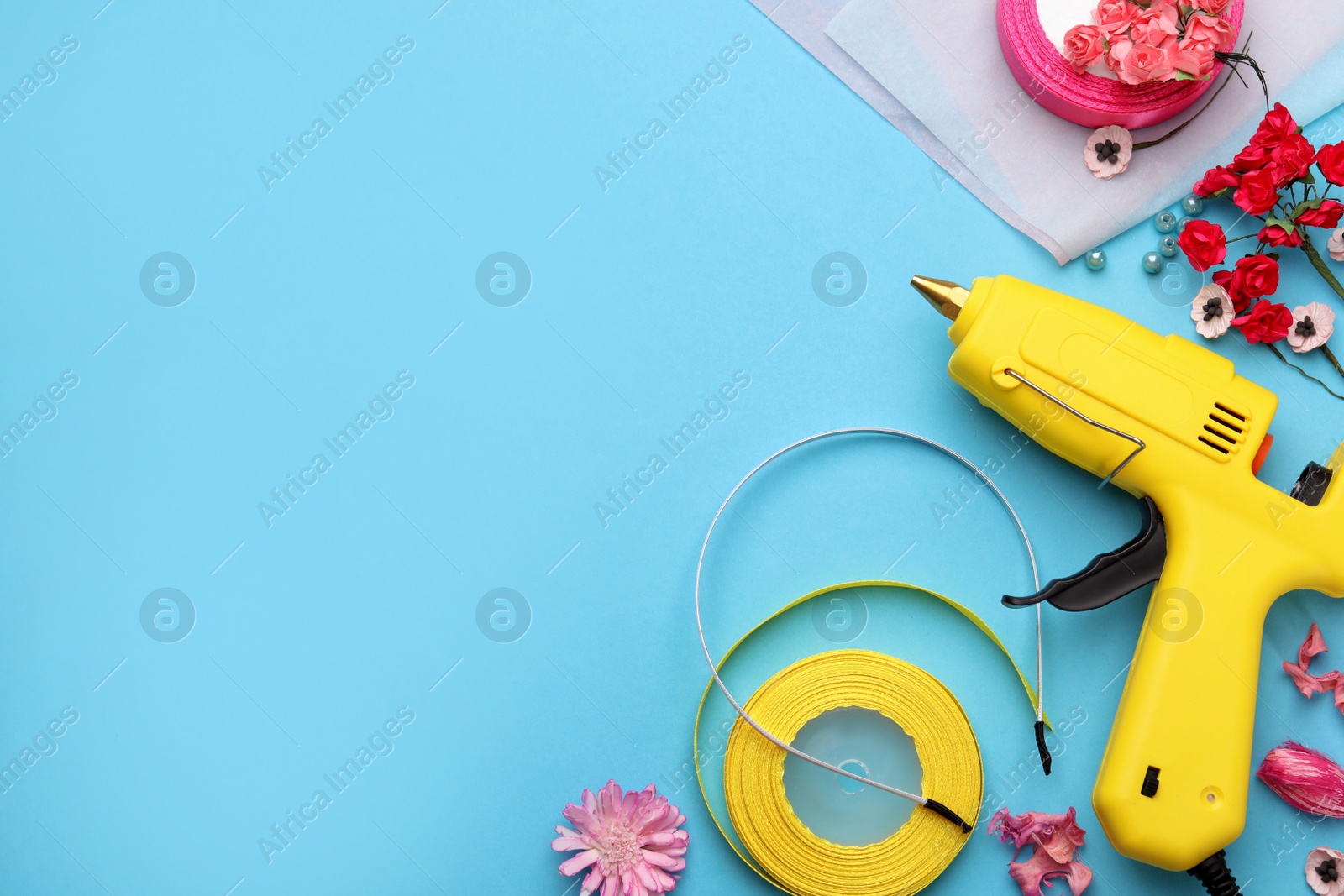 Photo of Hot glue gun, plastic headband and handicraft materials on light blue background, flat lay. Space for text