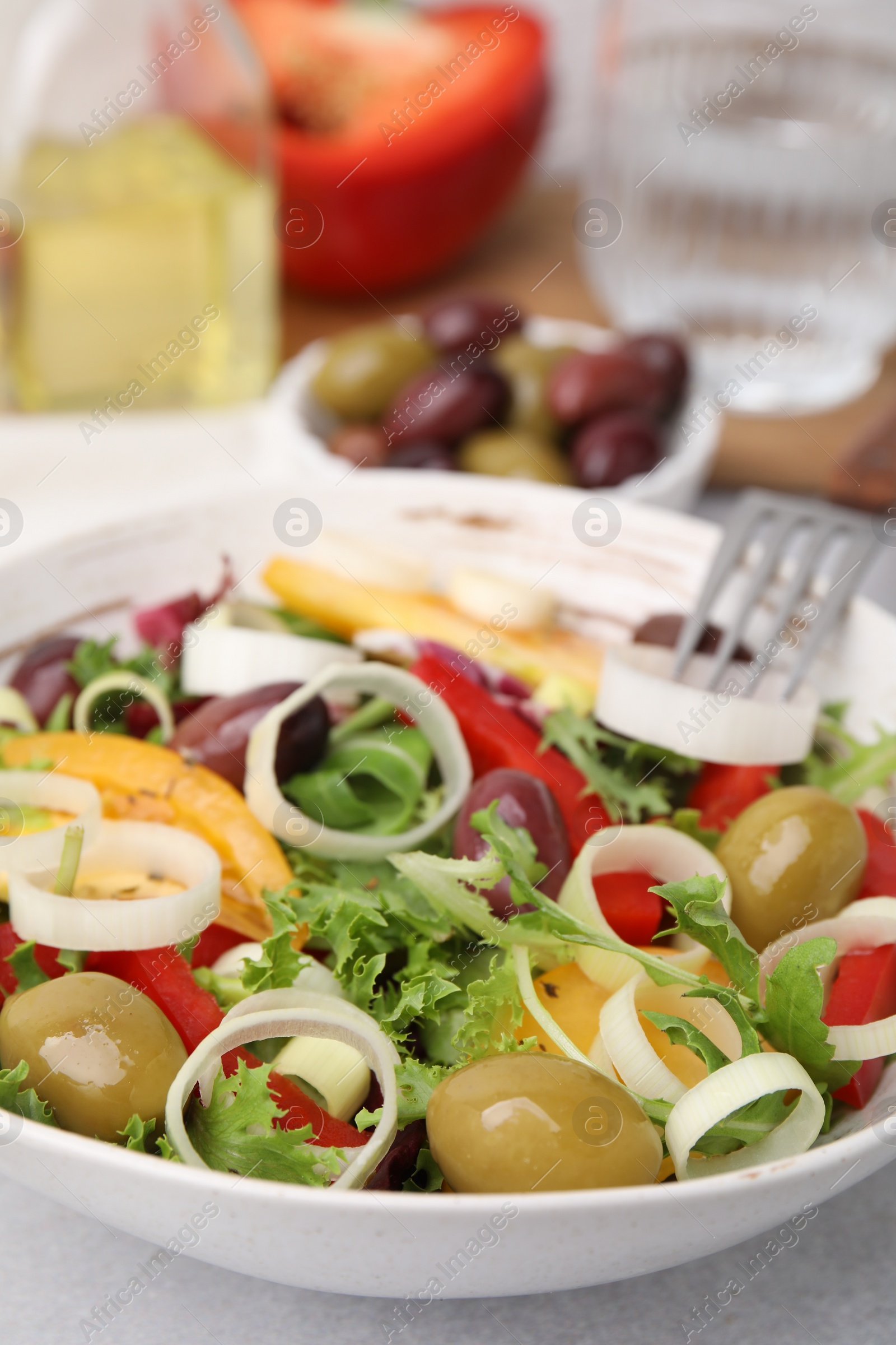 Photo of Bowl of tasty salad with leek and olives on light table, closeup