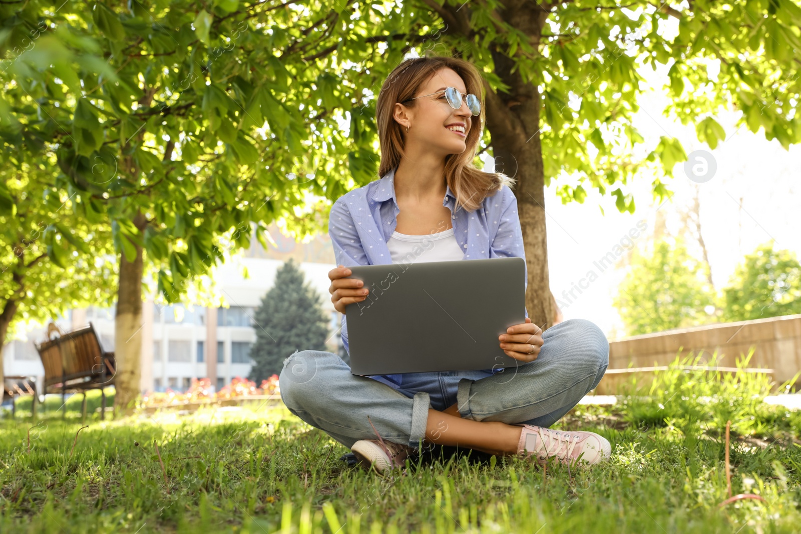 Image of Happy young woman with laptop sitting on green grass in park