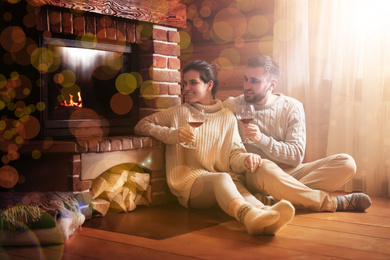 Image of Lovely couple with glasses of wine near fireplace at home. Winter vacation
