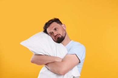 Photo of Unhappy man with pillow on yellow background. Insomnia problem