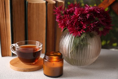 Photo of Beautiful pink chrysanthemum flowers, candle and cup of aromatic tea on light grey table