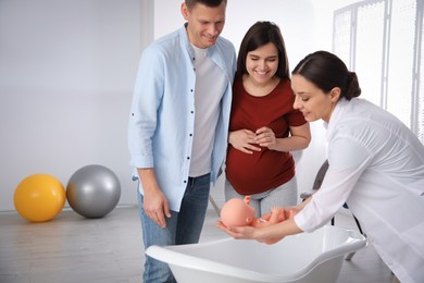 Photo of Man with pregnant wife learning how to bathe baby at courses for expectant parents indoors