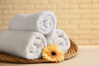 Photo of Rolled terry towels and flower on white table near brick wall indoors, closeup. Space for text