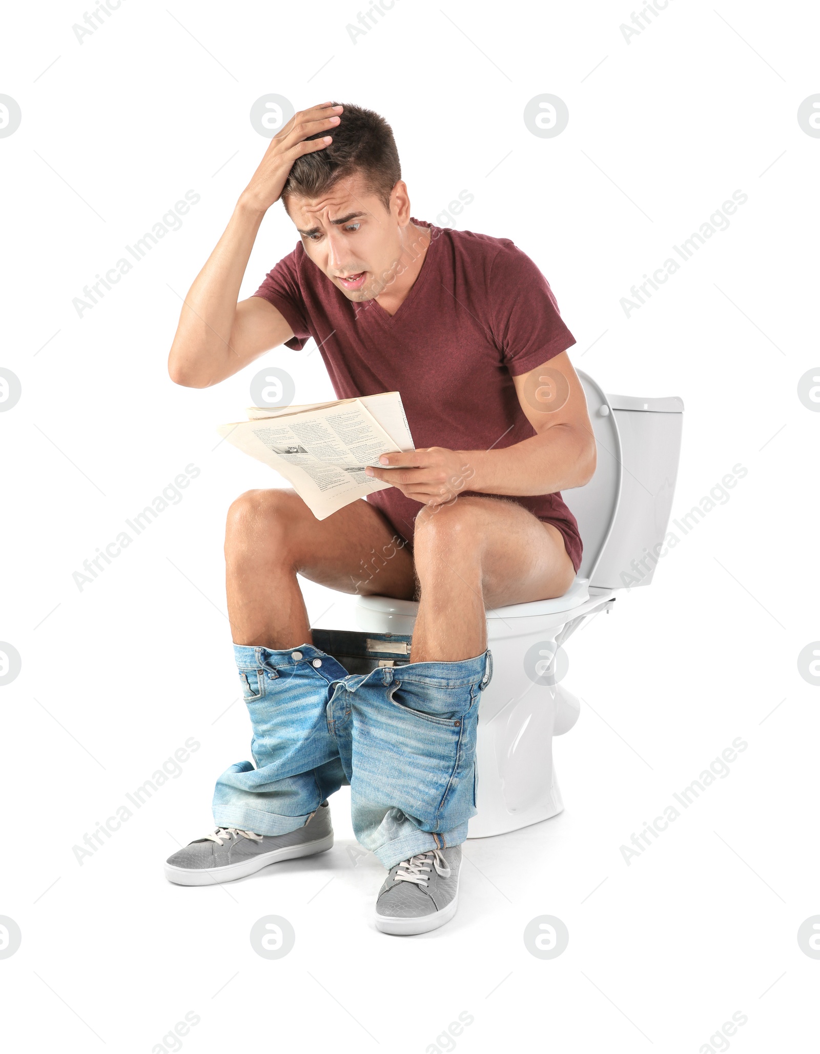 Photo of Young man reading newspaper while sitting on toilet bowl. Isolated on white