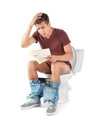 Young man reading newspaper while sitting on toilet bowl. Isolated on white