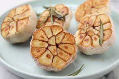 Photo of Heads of fried garlic and rosemary on plate, closeup