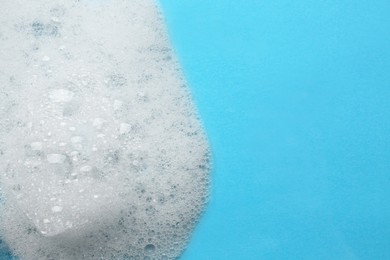 Photo of Fluffy bath foam on turquoise background, top view. Space for text