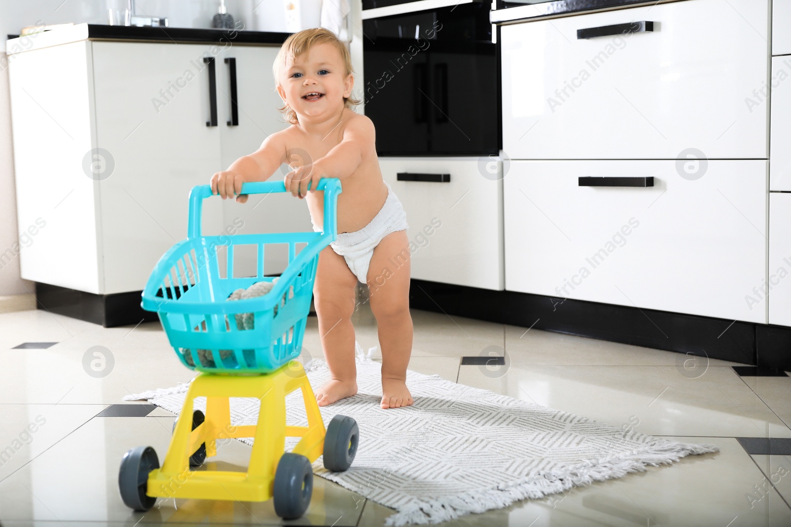 Photo of Cute baby with toy walker in kitchen. Learning to walk