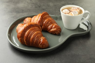 Tasty croissants served with cup of hot drink on grey textured table, closeup