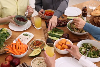 Friends eating vegetarian food at wooden table indoors, closeup