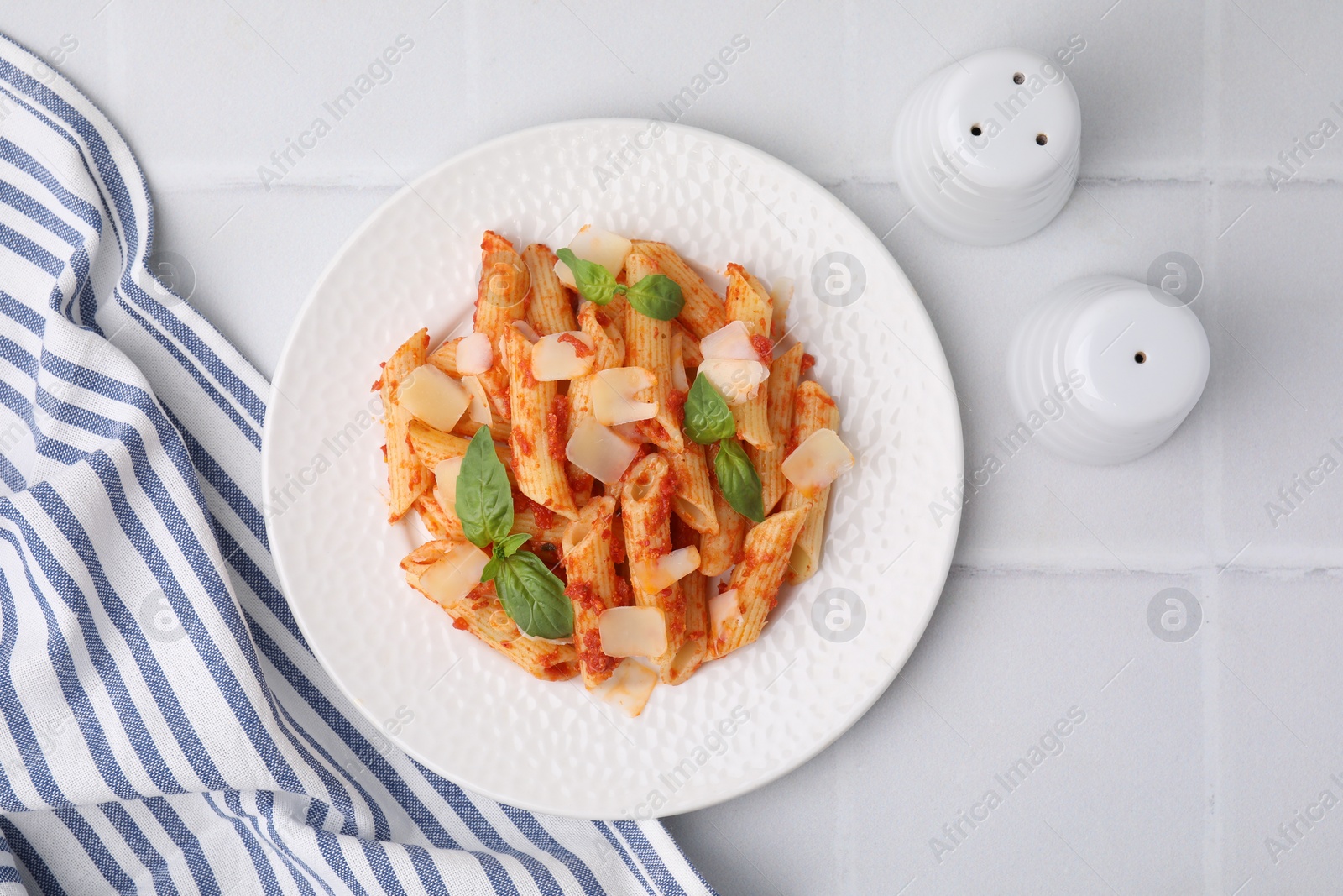 Photo of Tasty pasta with tomato sauce, cheese and basil on white tiled table, top view