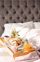 Tray with delicious croissants, cup of coffee and honey on bed