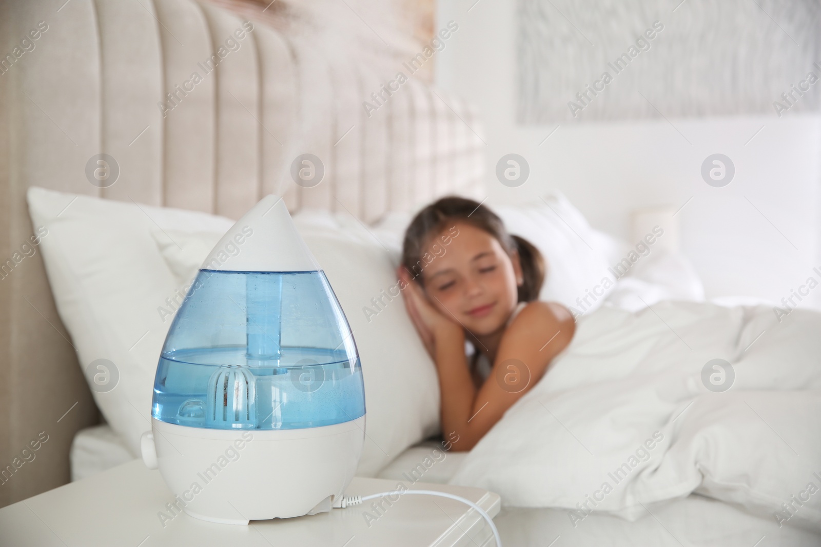 Photo of Cute little girl sleeping in bedroom with modern air humidifier