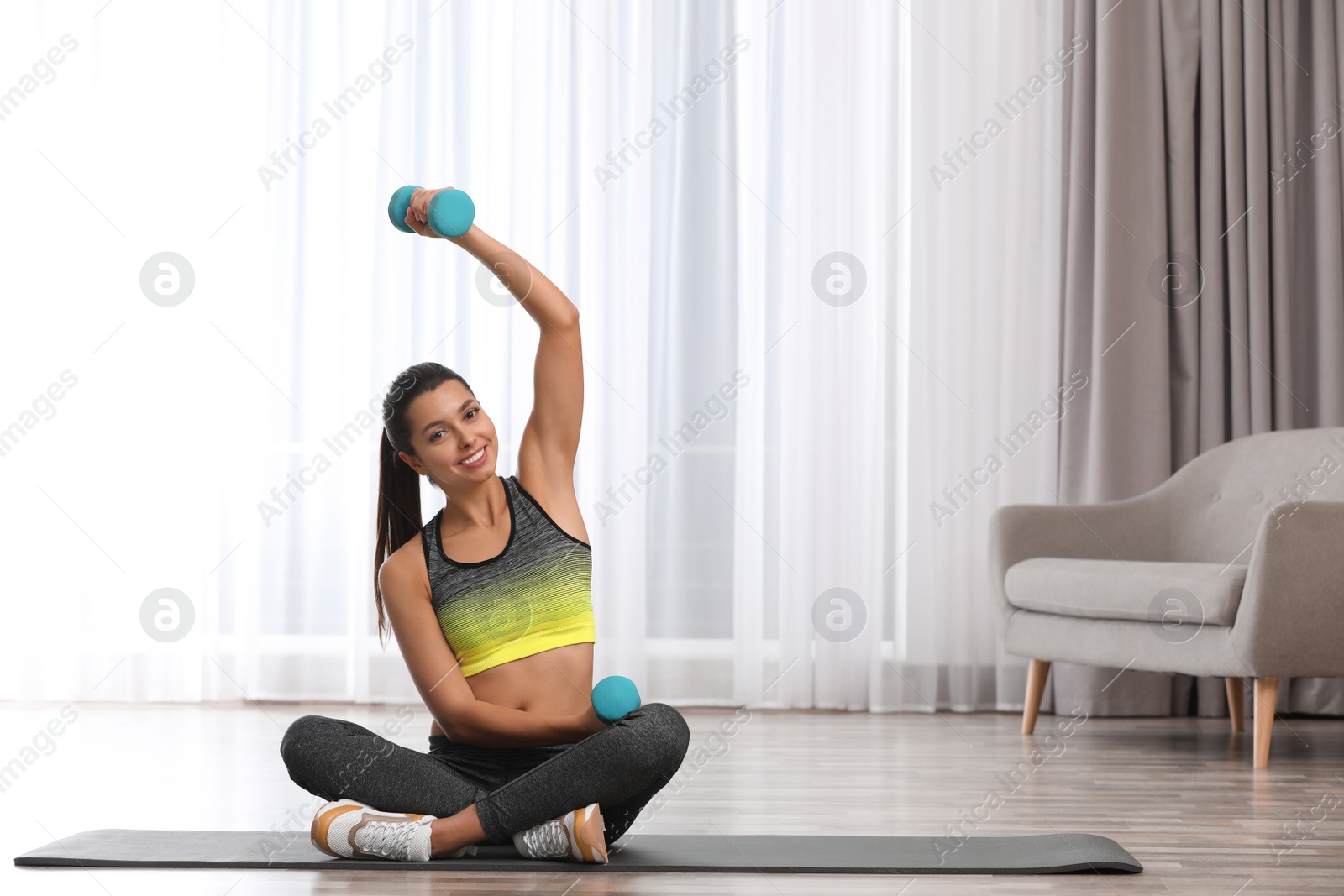 Photo of Young woman in fitness clothes doing exercise with dumbbells at home. Space for text