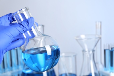 Doctor holding round bottomed flask with blue liquid, space for text. Laboratory analysis