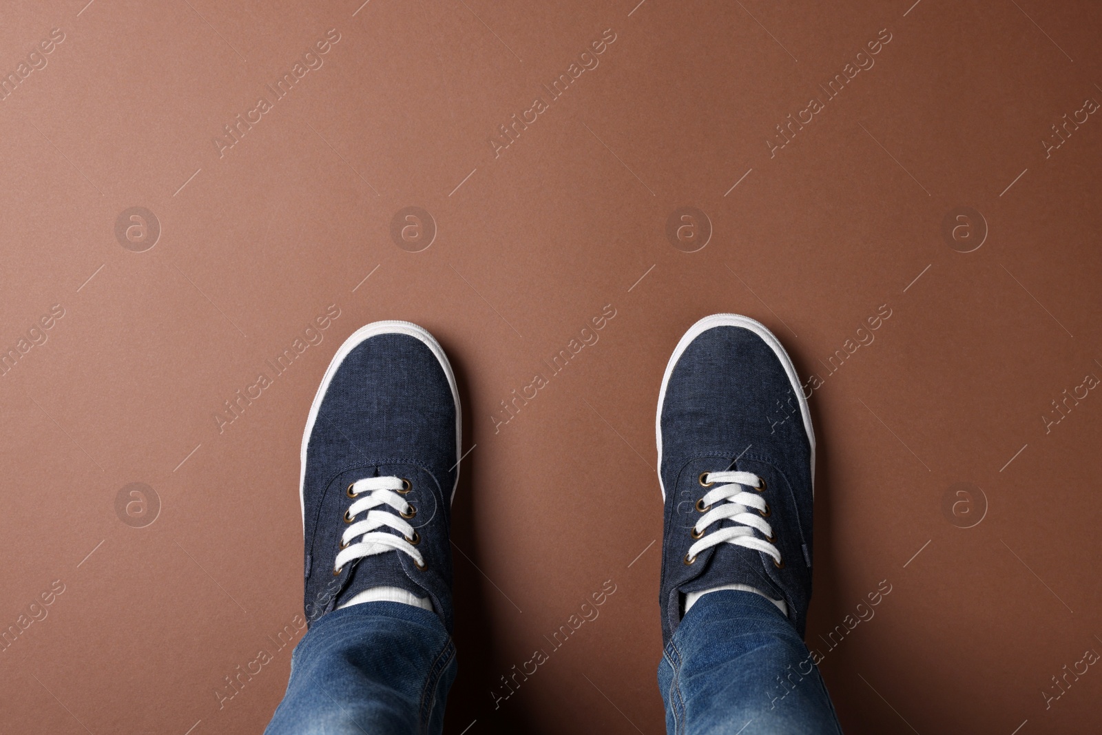 Photo of Child in stylish sneakers standing on brown background, top view