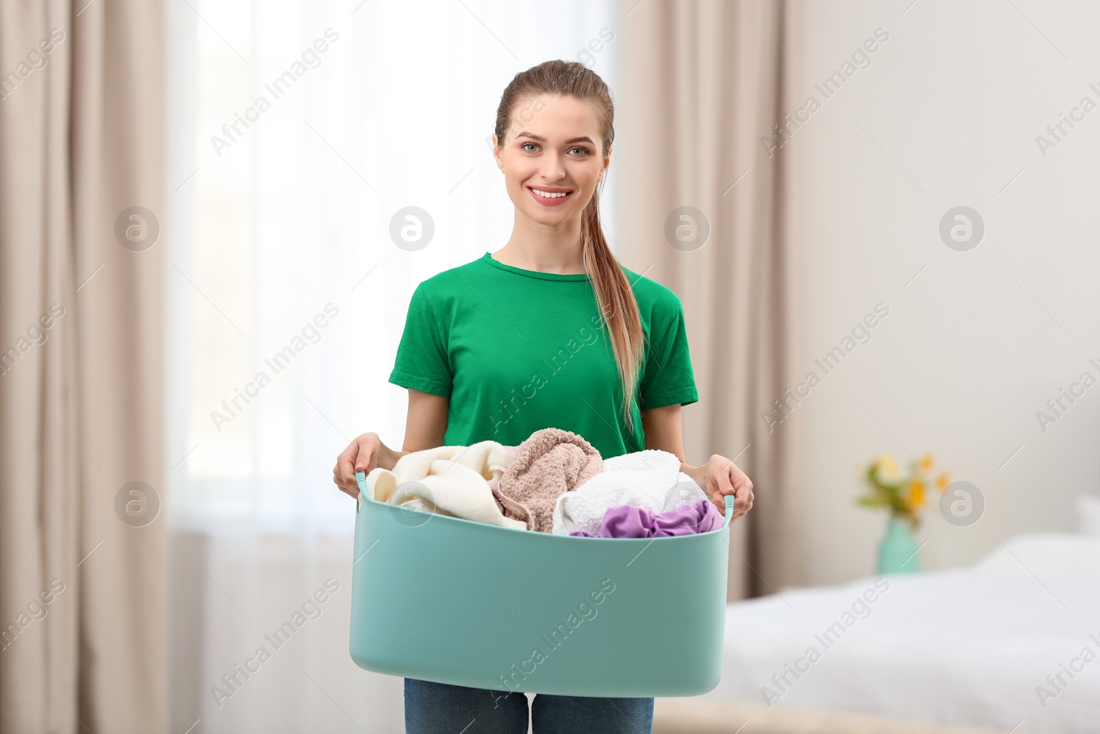Photo of Woman holding plastic basket with dirty laundry indoors