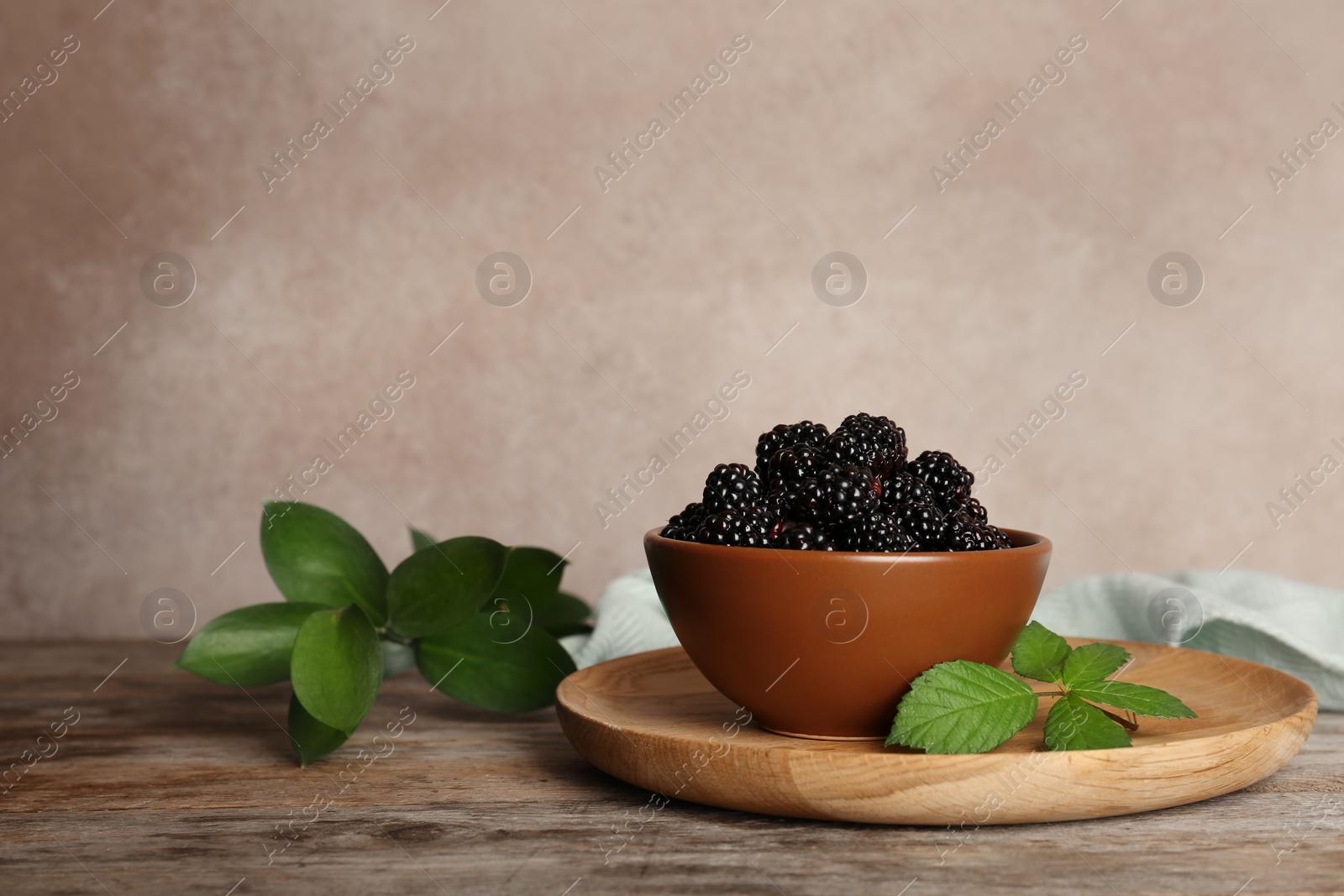 Photo of Bowl with fresh blackberry on wooden table against color background