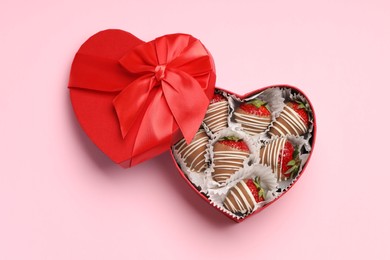 Photo of Heart shaped box with delicious chocolate covered strawberries on pink background, top view