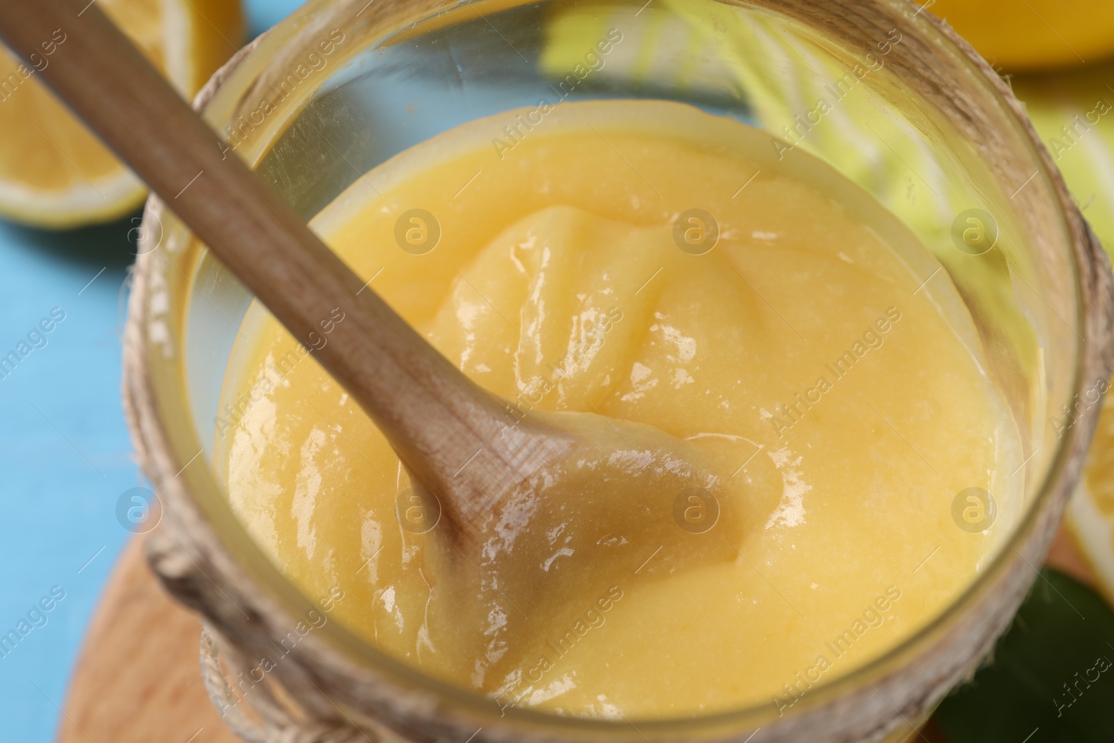 Photo of Delicious lemon curd in glass jar and spoon on light blue table, closeup
