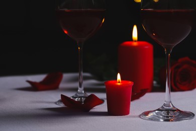 Photo of Glasses of red wine, rose flower and burning candles on white table, space for text. Romantic atmosphere