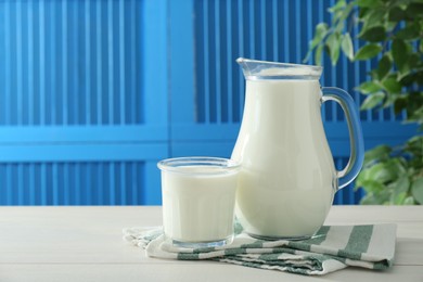 Jug and glass of fresh milk on white wooden table, space for text