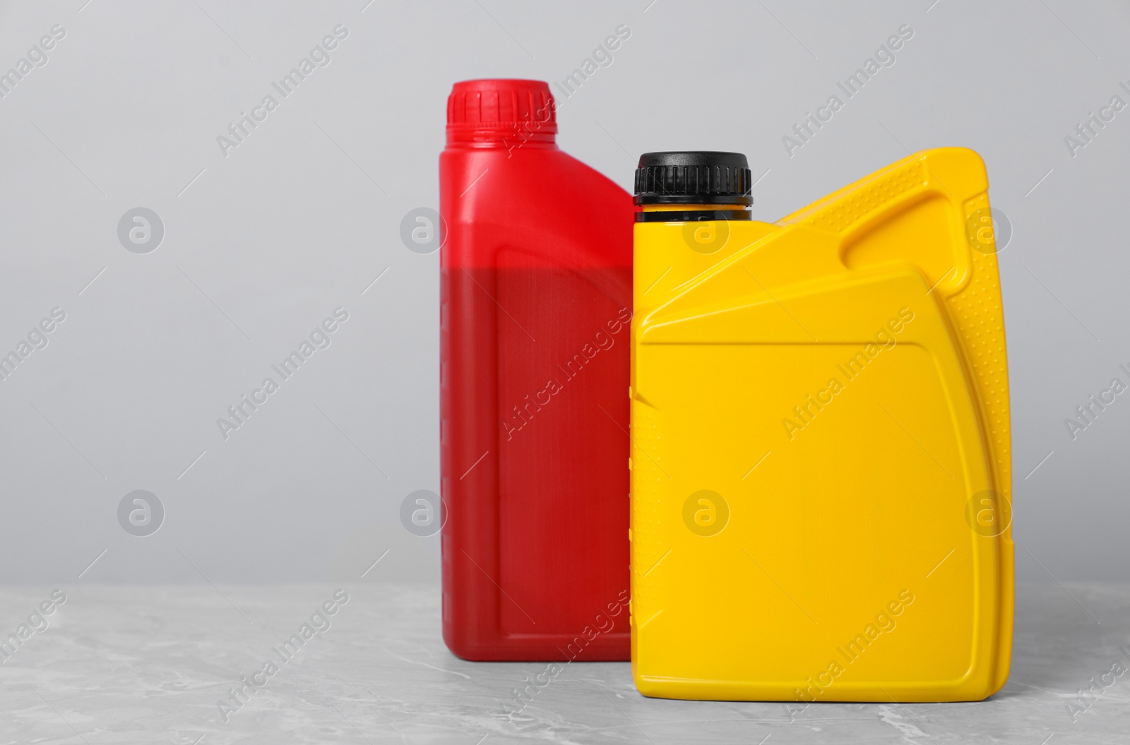 Photo of Motor oil in different canisters on grey marble table against light background, space for text