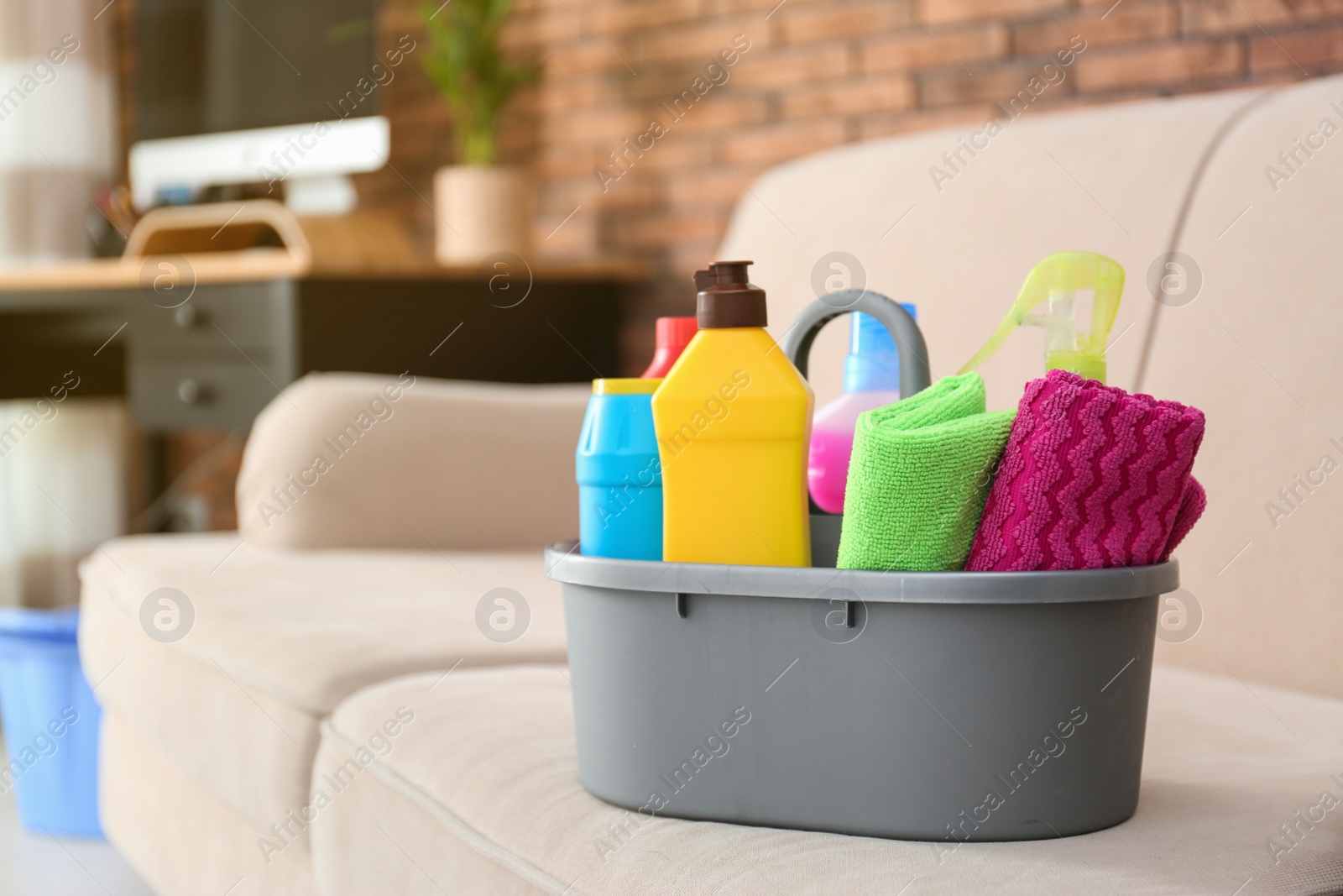 Photo of Basin with different detergents on sofa indoors, space for text. Cleaning service