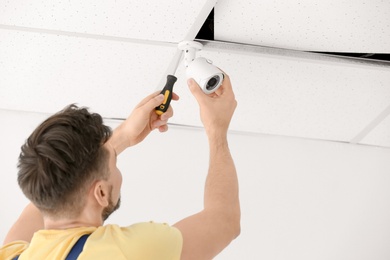 Technician installing CCTV camera on ceiling indoors