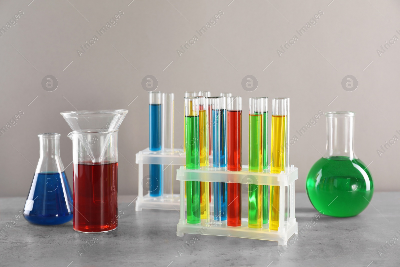 Photo of Test tubes with liquids in stand and flasks on table against light grey background